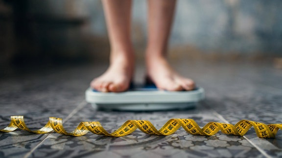 Frauenfüße auf einer Waage, davor ein Maßband