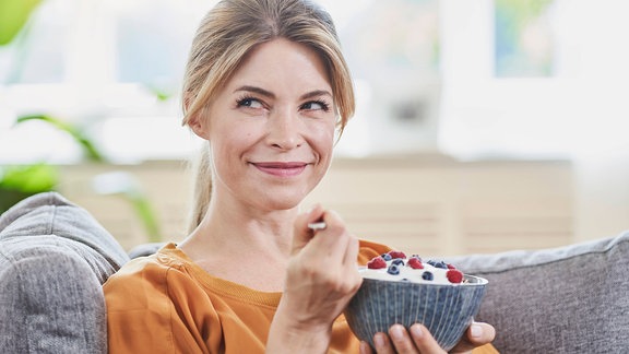 Eine Frau sitzt auf einem Sofa und isst einen selbstgemachten Jogurt.
