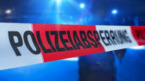 Absperrband vor einem Polizeieinsatz mit Blaulicht. 