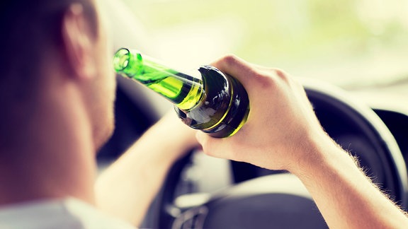 Ein Mann hebt am Steuer eines Autos eine Flasche zum Mund