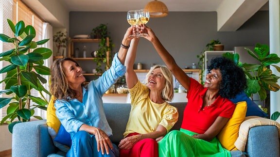 Drei Frauen lachen gemeinsam und schauen auf Gläser mit Alkohol. (verharmlosender Alkohol-/Drogenkonsum)