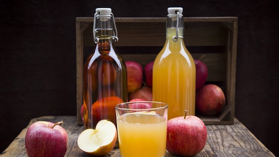 Zwei Flaschen und ein Glas mit Apfelsaft und Äpfel