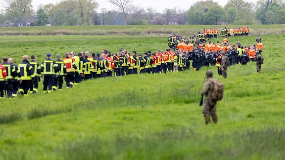 Soldaten der Bundeswehr und Einsatzkräfte von Feuerwehr und Polizei stellen sich auf, um ein Feld abzusuchen.