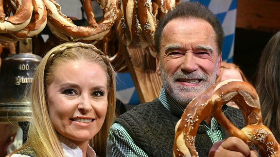 Arnold Schwarzenegger und seine Freundin Heather Milligan halten lächelnd Brezeln in die Kamera
