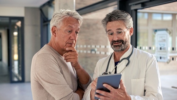 Lächelnder Oberarzt diskutiert mit Mann im Krankenhausflur.
