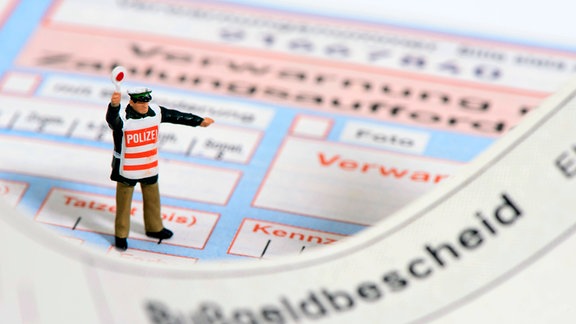 Ein Modell-Polizist steht auf einem Bußgeldbescheid und Verwarnungszettel.