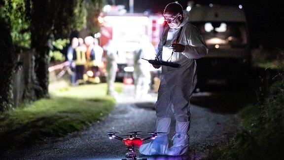 Ein Mitarbeiter der Spurensicherung steht mit einer Drohne auf einem Waldweg.