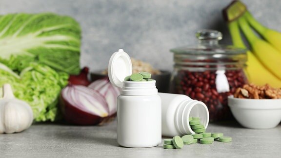 Flasche mit grünen Pillen, im Hintergrund Obst und Gemüse