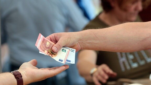 Frau reicht einer Marktverkäuferin Bargeld zum Bezahlen ihrer gekaufter Ware.