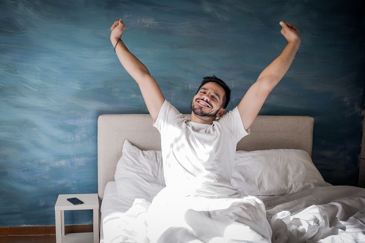 Ein Mann streckt sich in einem Bett.