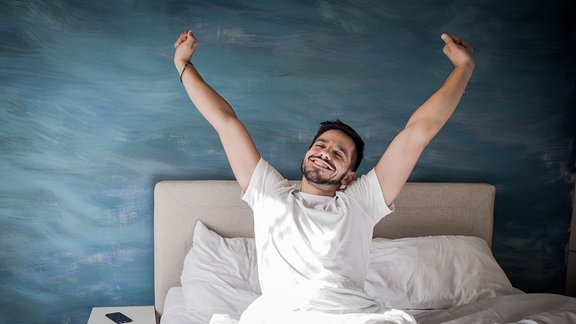 Ein Mann streckt sich in einem Bett.
