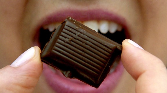 Ein Stück Schokolade hält eine junge Frau in der Hand.