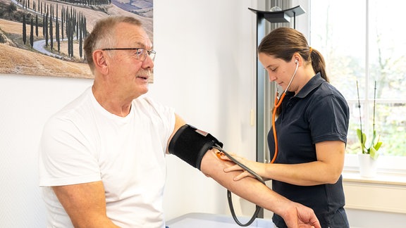Eine Sprechstundenhilfe misst den Blutdruck am Arm eines aelteren Patienten