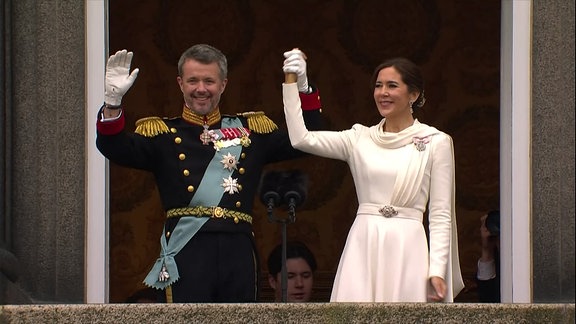 Königin Mary von Dänemark und ihr Ehemann winken einer Menge zu.