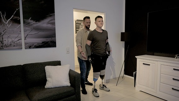 Ein Junge mit Bein- und Armprothesen läuft durch eine Tür.