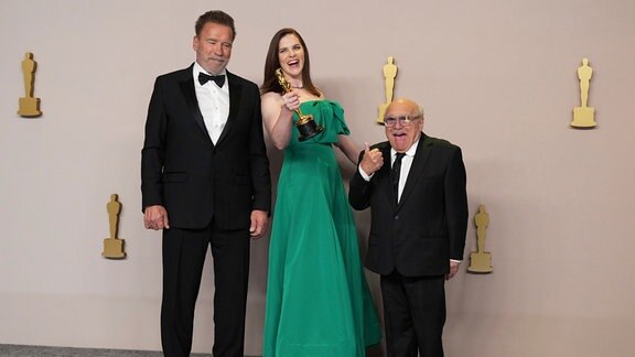 Jennifer Lame, Mitte, Gewinnerin des Preises für den besten Filmschnitt für "Oppenheimer", posiert im Presseraum mit Arnold Schwarzenegger, links, und Danny DeVito bei der Oscar-Verleihung.