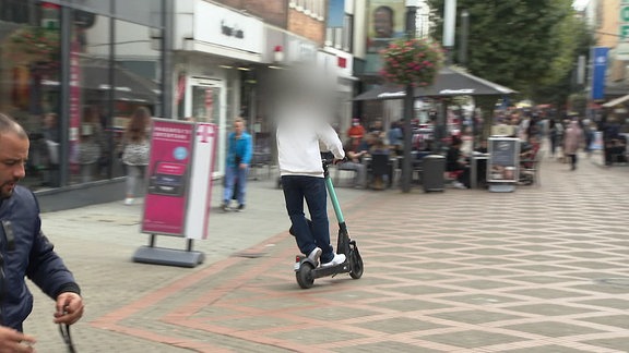 Eine Person fährt mit einem E-Roller durch eine Innenstadt.