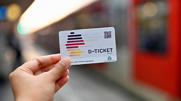 Eine Person hält ein Deutschlandticket in die Kamera.