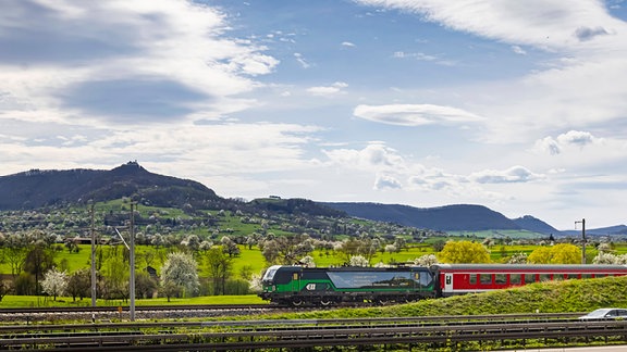 Landschaftsaufnahme mit einem Zug, der durchs Bild fährt.