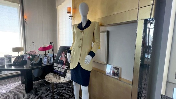 Eine Figur mit einem Gelb-Blauen modischen Outfit steht in einem Raum mit weiteren Dingen.