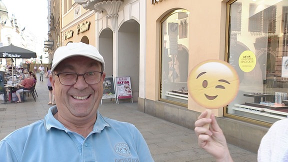 Frau hält Stock mit Zwinker-Emoji neben einen Mann der ebenfalls zwinkert