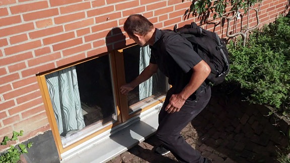 Ein fachkundiger Mann überprüft ein Kellerfenster eines Wohnhauses