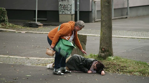 Eine Passantin schaut nach einer Person die auf dem Boden liegt.