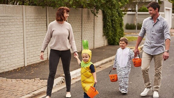 Zwei Erwachsene und zwei Kinder laufen händehaltend über eine Straße.