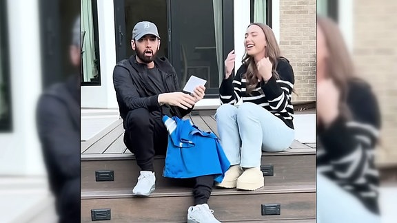Rapper Eminem schaut sehr überrascht in die Kamera während seine Tochter neben ihm sitzt und lacht.