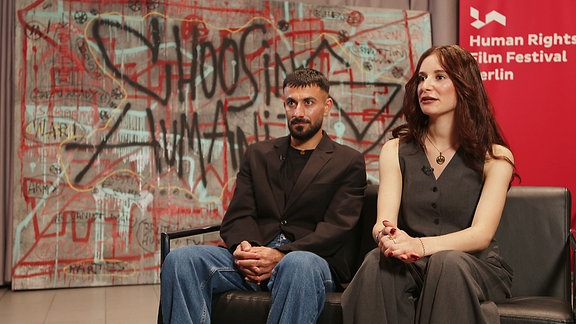 Die Geschwister Leila und Tahsim sitzten auf einer Couch.