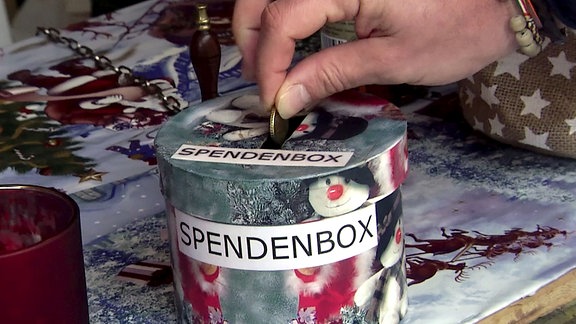Eine Hand wirft Kleingeld in eine Spendenbox