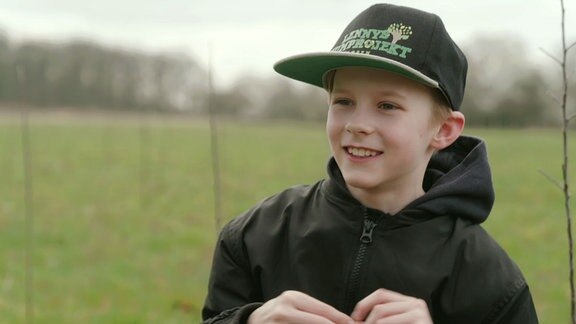 Ein Junge steht lächelnd vor einem Feld mit jungen Bäumen.