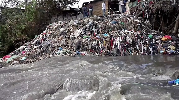 Müll türmt sich am Ufer eines Wasserlaufs.