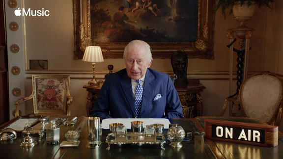 König Charles sitzt an einem Tisch und spricht in die Kamera.