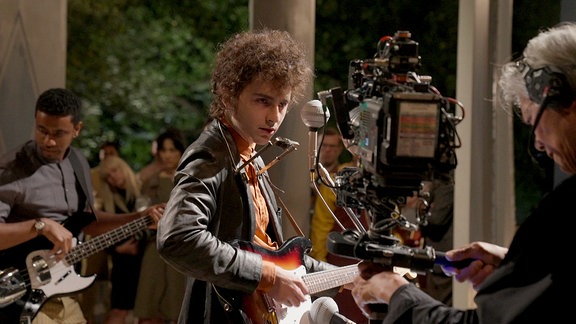 Filmstill: Bob Dylan-Darsteller mit Gitarre und Mundharmonika