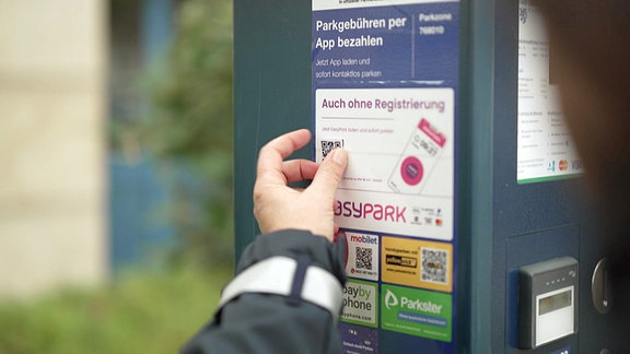 Eine Hand greift an einen QR-Code auf einer Parksäule