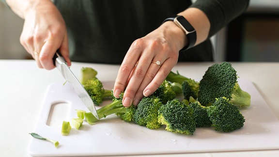 Frauenhände schneiden Brokkoli in der Küche