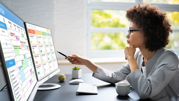 Eine Frau vor zwei Monitoren schaut auf einen Digitalen Kalender.