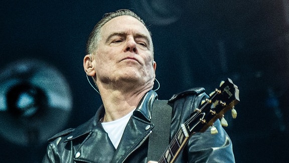 Bryan Adams mit Lederjacke und einer Gitarre auf der Bühne.