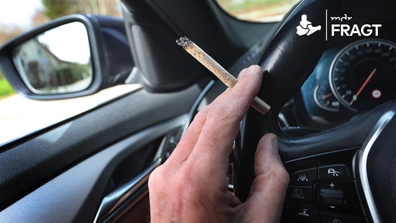 Ein Mann sitzt mit einem Joint zwischen den Fingern am Steuer eines Autos.