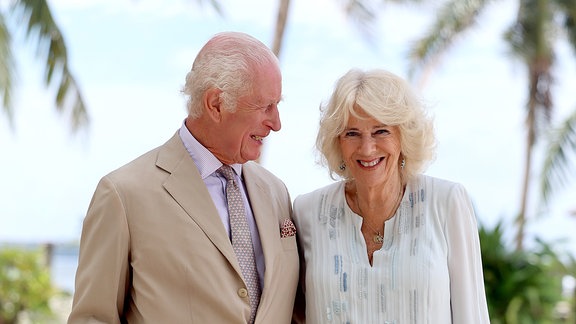 König Charles III. und Königin Camilla lächeln während eines Strandbesuchs.