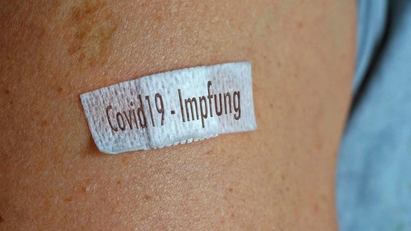 Ein kleines Pflaster mit der Aufschrift Covid19-Impfung auf einem Oberarm