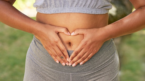 Eine Frau hält sich mit beiden Händen den Bauch.