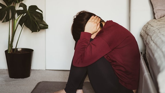 Depressive und traurige Frau, die ihren Kopf mit den Händen bedeckt und auf dem Boden im Schlafzimmer sitzt. 