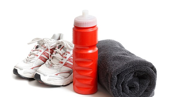 Sportschuhe stehen neben einer Trinkflasche und einem zusammengerolltem Handtuch.