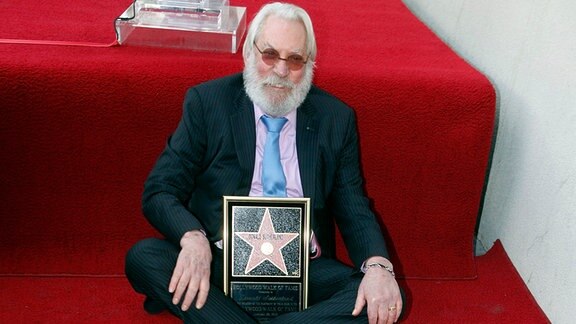 Donald Sutherland sitzt auf einem Roten Teppich vor seinem Stern auf dem Walk of Fame.