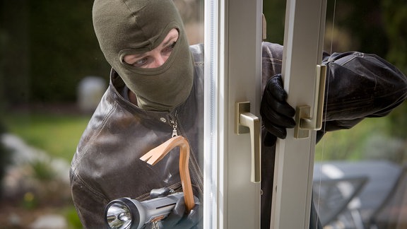Ein Einbrecher bricht über das Fenster in ein Haus ein. (Symbolbild)
