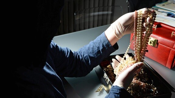 Einbrecher begutachtet eine Schatulle mit Schmuck