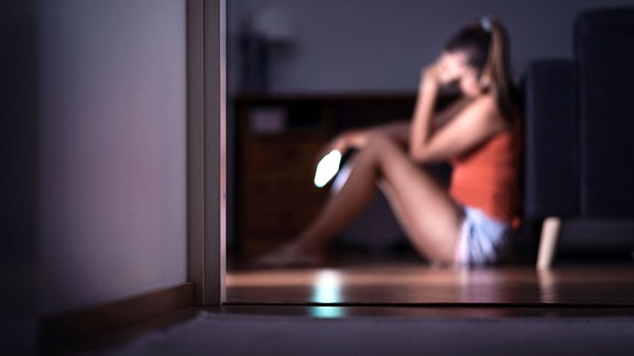 Trauriger Teenager mit Smartphone in ihrem Zimmer auf dem Boden sitzend.