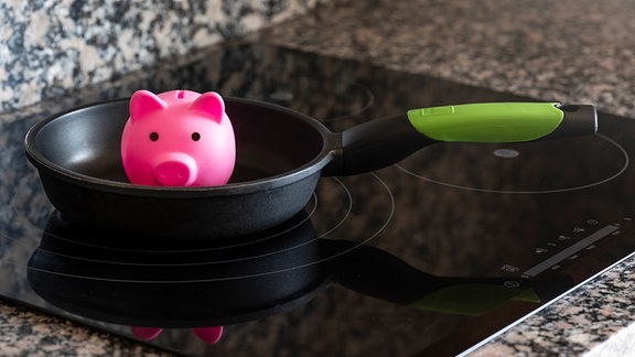 Ein Sparschwein steht in einer Pfanne auf einem Herd.